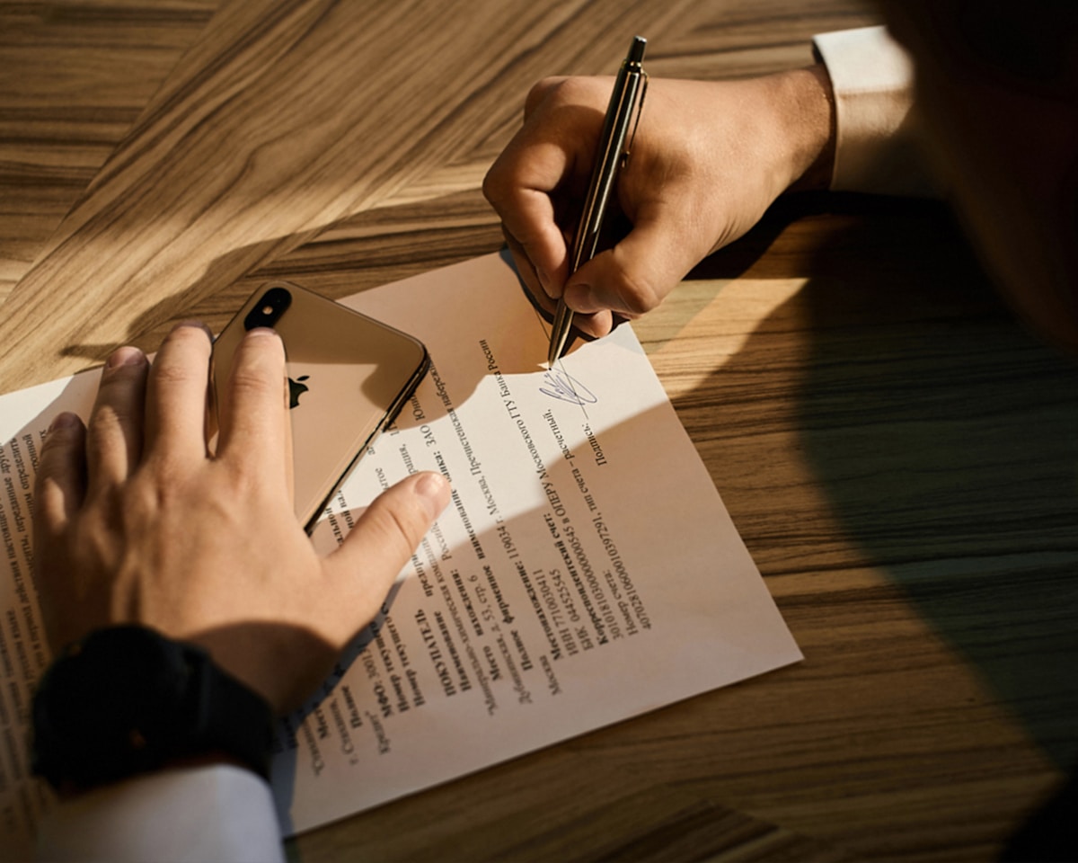 A close-up of a person signing a document at a wooden desk